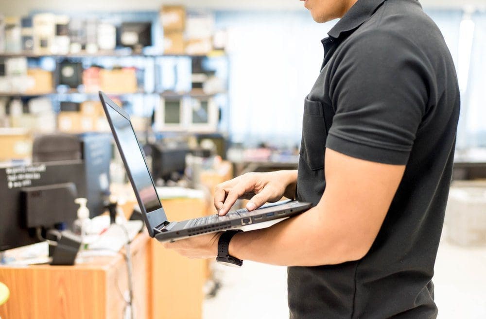 IT-support-technician-stands-holding-a-laptop-in-an-open-office-space